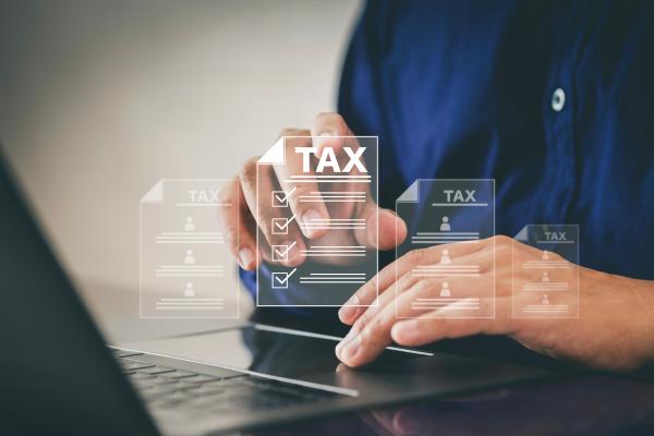 Close up of hands using a laptop on a desk, with virtual checklist images projected above, headed "Tax"