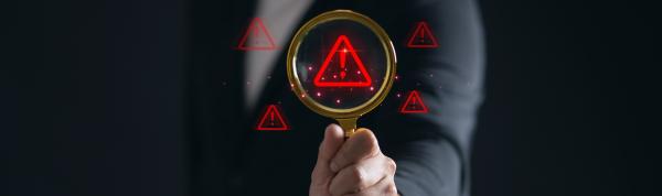 Man in suit holding a magnifying glass over a red exclamation mark warning symbol 