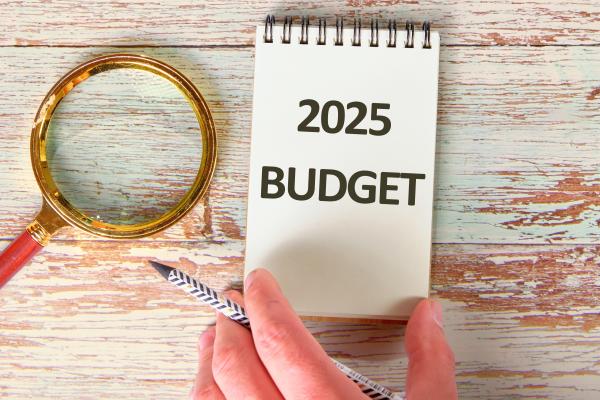 Open notepad on desk with "2025 Budget" written on it, next to magnifying glass