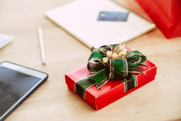 Small red box wrapped with green and gold ribbon, on a desk with stationery around it