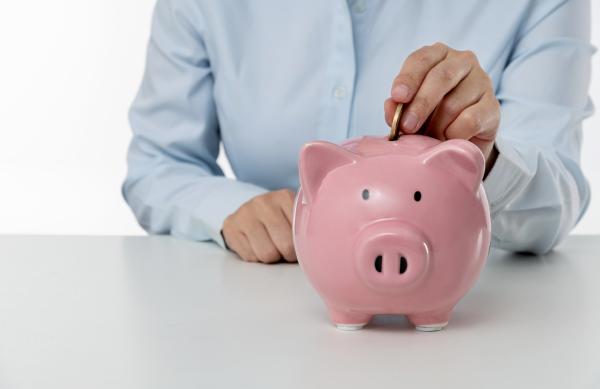 Piggy bank on desk with person putting a coin in the top