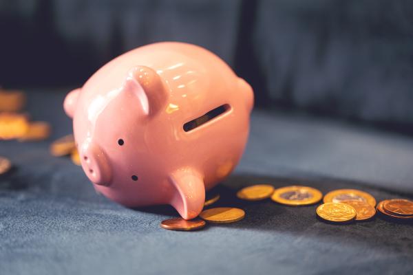 A pink piggy bank is lying on its side with scattered coins around. 
