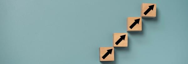 Wooden blocks with black arrows showing an upward trajectory on a grey background