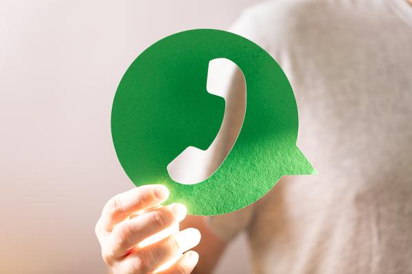 A man is holding up an oversized cardboard cut out of a 'contact us' icon which has a phone cut out of a green circle