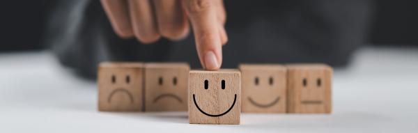 Row of 5 wooden blocks, the middle one shows a happy face, the others sad faces,  A finger is pushing forward the block with the happy face