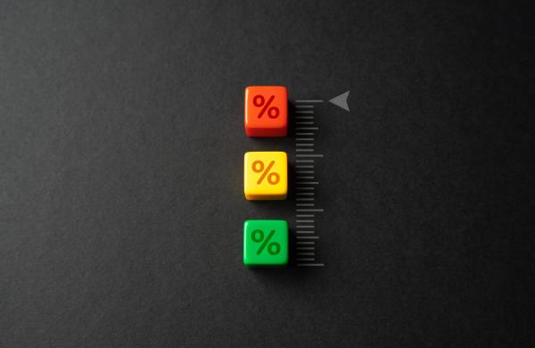A red, yellow and green block, each with a percentage symbol stamped on the side, stand on top of each other on a black background