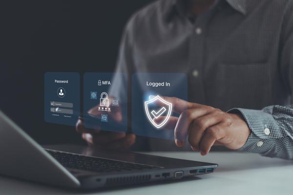 A man sits waiting to log into his laptop, with icons in front of him showing a password box, then the MFA box and then a tick for logged in. Intended to show the process of logging in. 