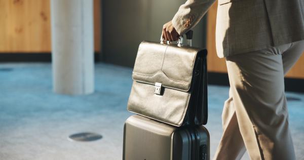 Businessman in suit pushing wheeled suitcase with a leather briefcase on top of it