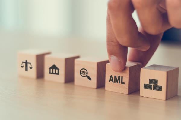 A row of wooden cubes with a hand selecting the one with AML written on it