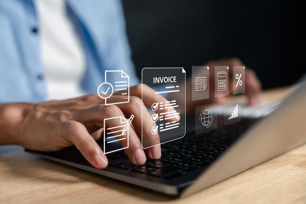 Hands using a laptop, with virtual graphics appearing over the keyboard, one of which reads "Invoice"