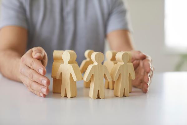 Wooden people arranged in a circle on a flat surface, with person's hands surrounding them 