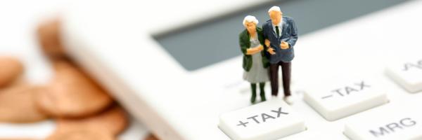 Image of a miniature model of an elderly couple on top of a calculator with the word tax on the buttons