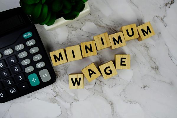 Wooden blocks spelling out "minimum wage" on a worktop next to a calculator