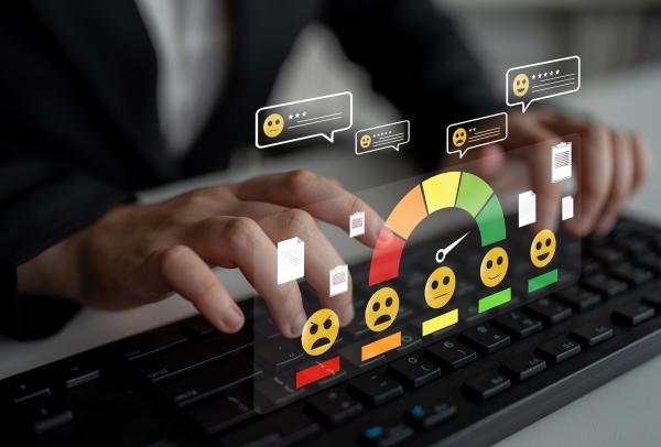 Virtual graphics of a row of five smiley faces ranging from angry to happy projected above a person's hands typing on a keyboard 