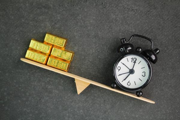 Tilting balance beam with gold bars on the upward end and an alarm clock on the downward end