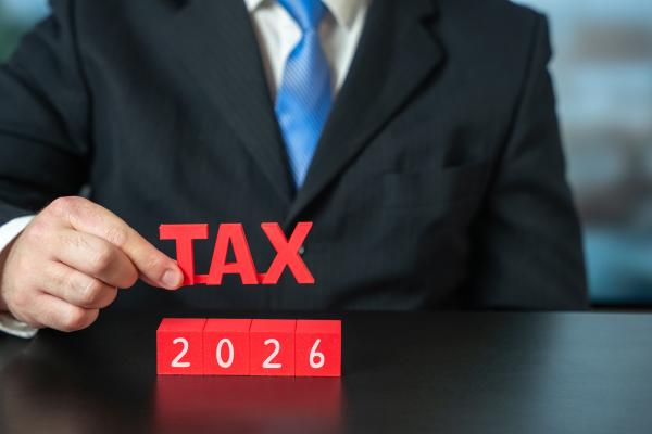 Man in suit holding the word TAX over blocks reading 2026