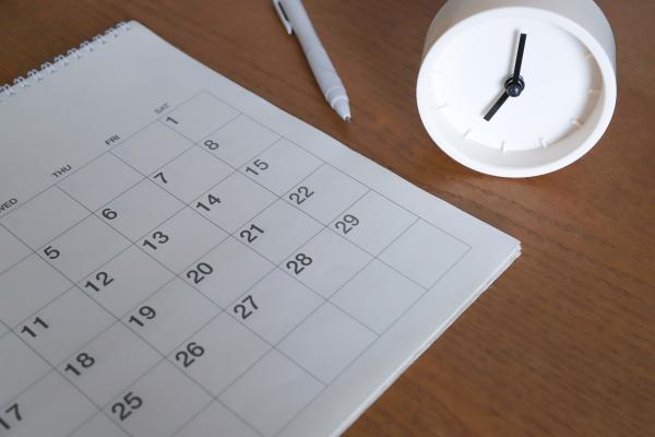 Calendar on a desk next to an analogue clock and a pen