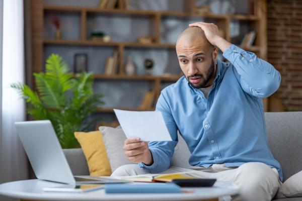 Man sat on sofa reading piece of paper and looking shocked and worried