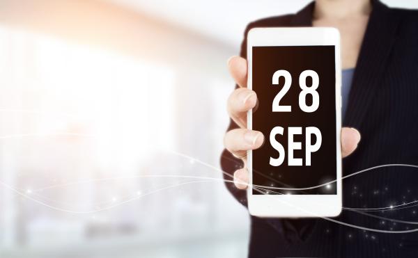 A woman holds up a mobile phone with the date 28 September in bold print