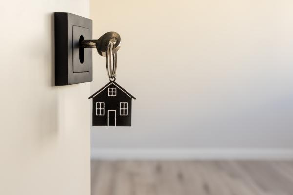A key is resting in the lock of a house door. The key fob is in the shape of a house to symbolise home ownership
