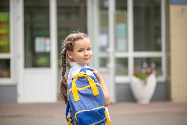 Young girl in school uniform carrying a rucksack looking over her shoulder as she walks into school