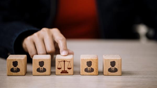 Five wooden cubes in a row, finger pointing to the middle one which shows scales of justice. The other four show a profile of a person