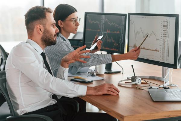Smartly dressed man and woman working at desk together looking at charts on screens