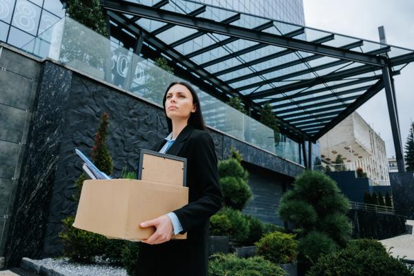 Smartly dressed woman outside office building carrying a cardboard box of her possessions