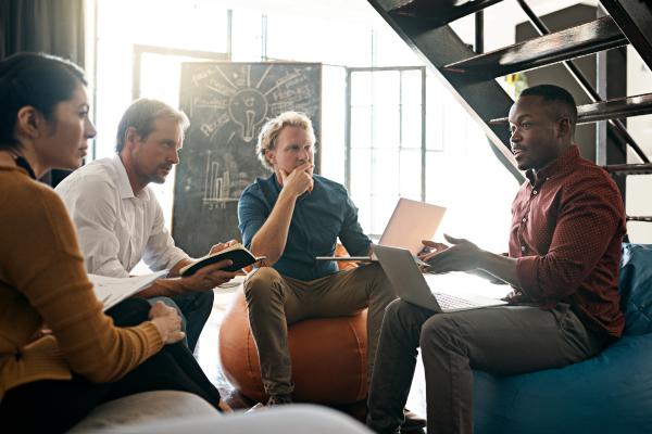 Smartly dressed people sat in a group, comparing notes with an ideas blackboard in the background